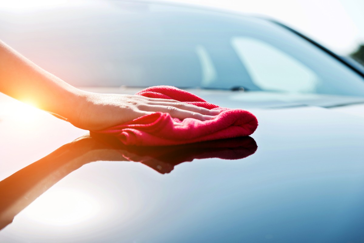 Detailaufnahme einer Hand, die eine Motorhaube mit einem Lappen sauber macht