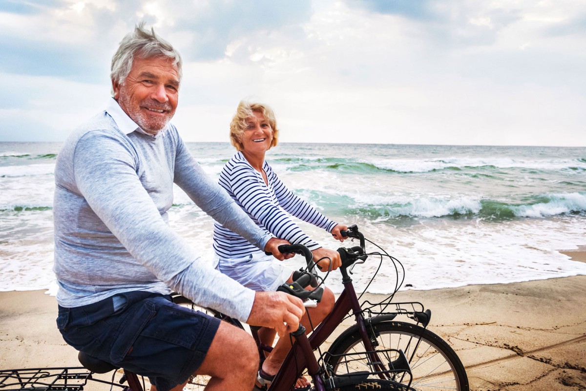 Älteres Ehepaar fährt auf E-Bikes am Strand
